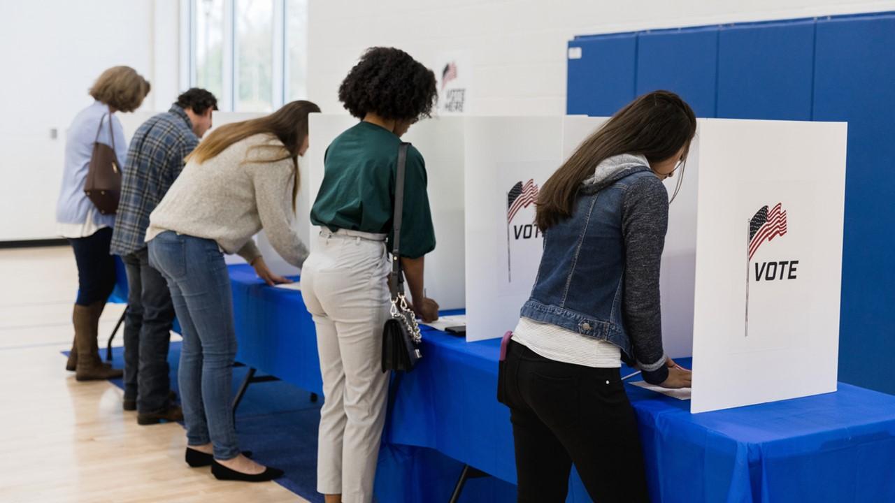 People line up at table with a blue table cloth to cast their vote privately.