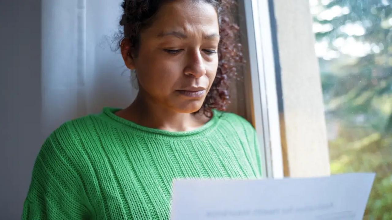 A concerned woman wearing a green sweatshirt reviews correspondence from the IRS. 