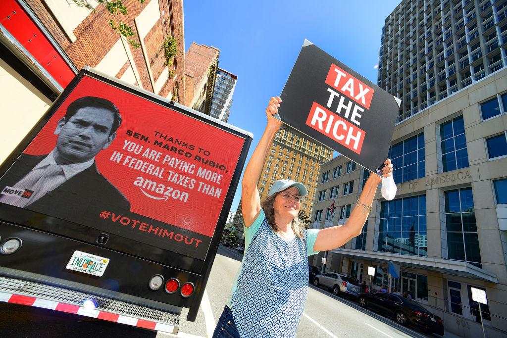 A woman holding up a sign about taxing the rich.