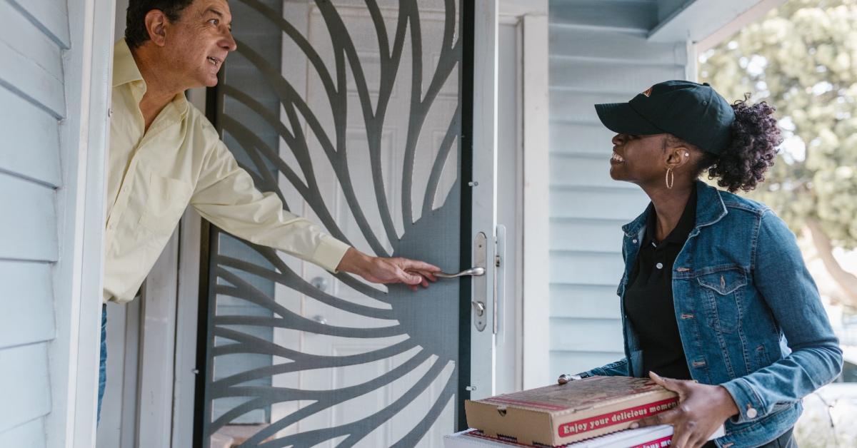 A customer greets a pizza delivery girl holding pizza at the door.