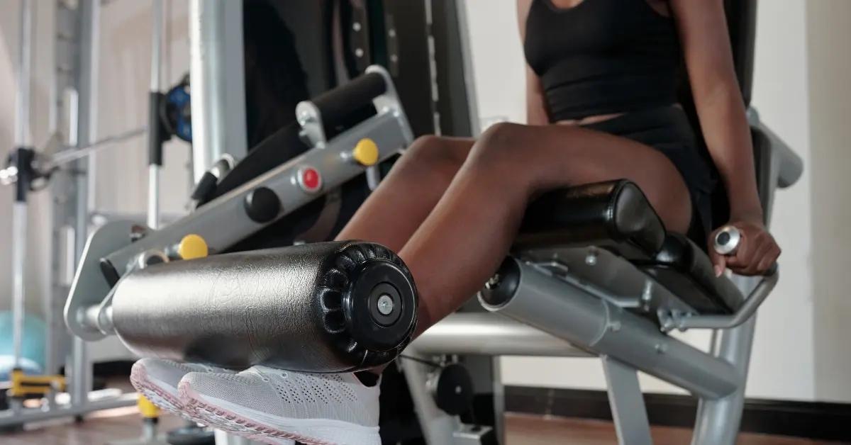 A woman in black workout attire uses a leg machine at the gym.