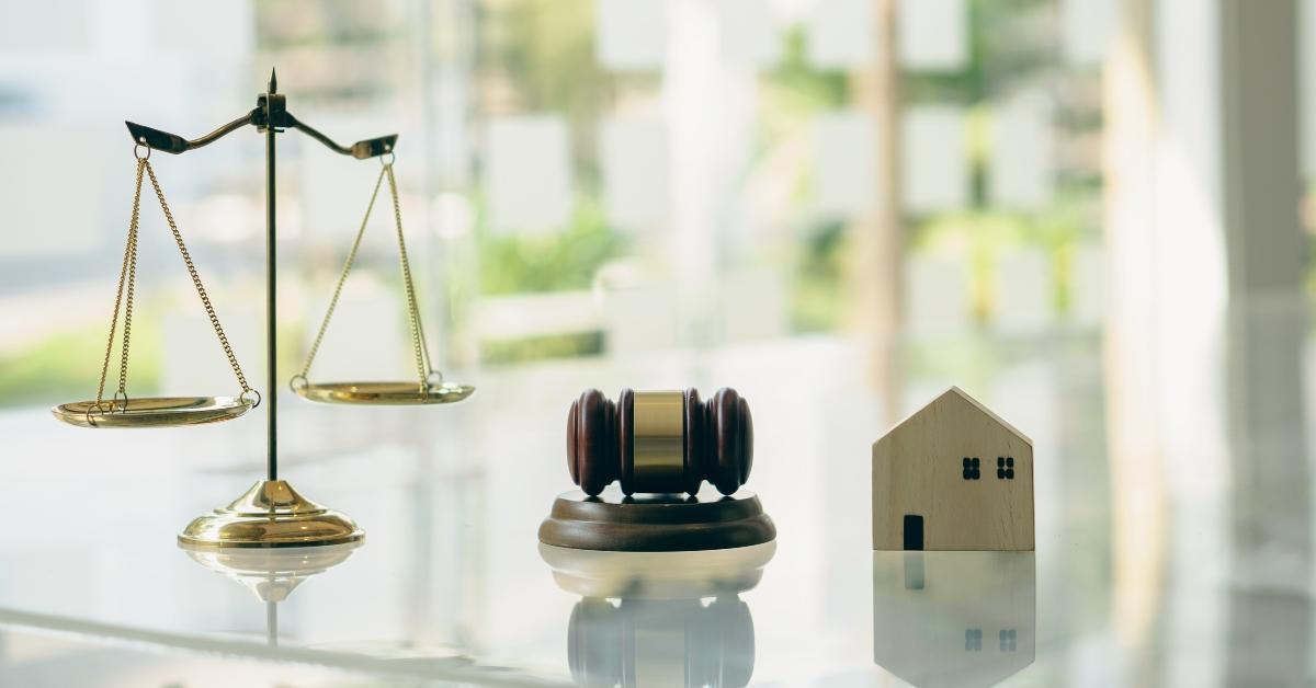 A court weight scale, gavel, and small wooden home on a table