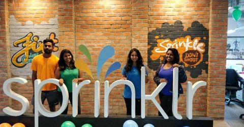 Sprinklr employees standing behind sign in office