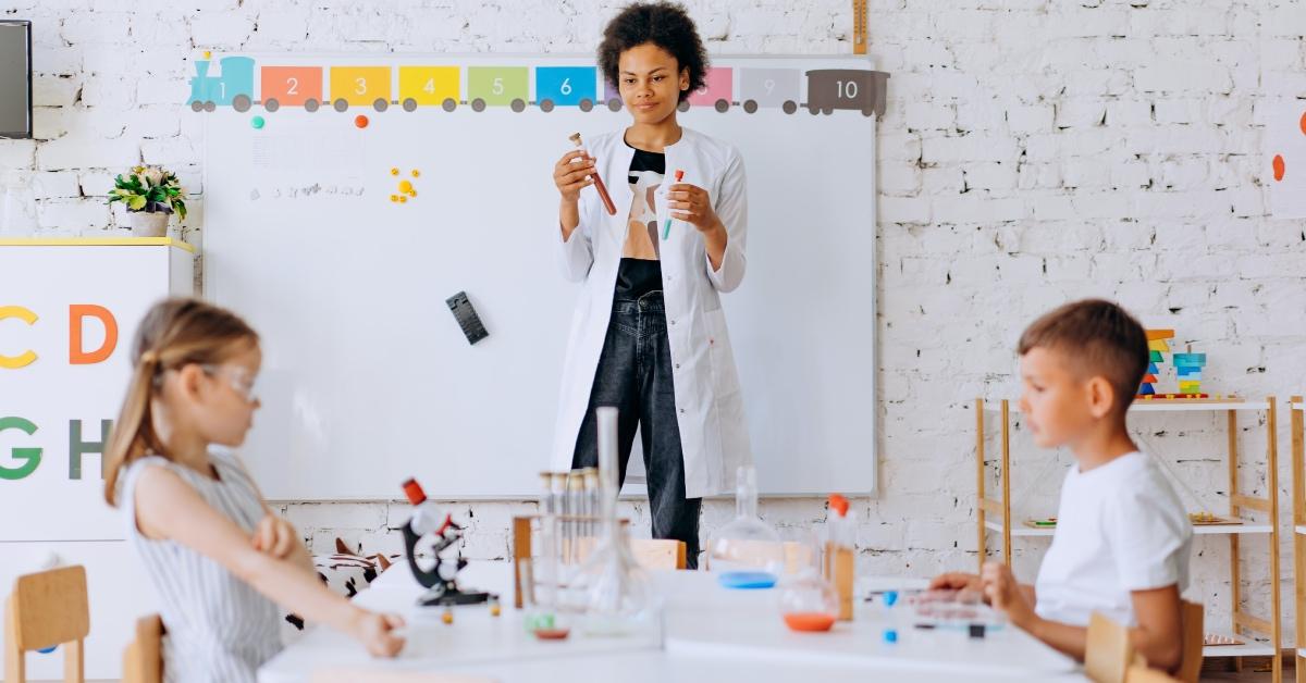 A young elementary school teacher in a lab coat experimenting with students.