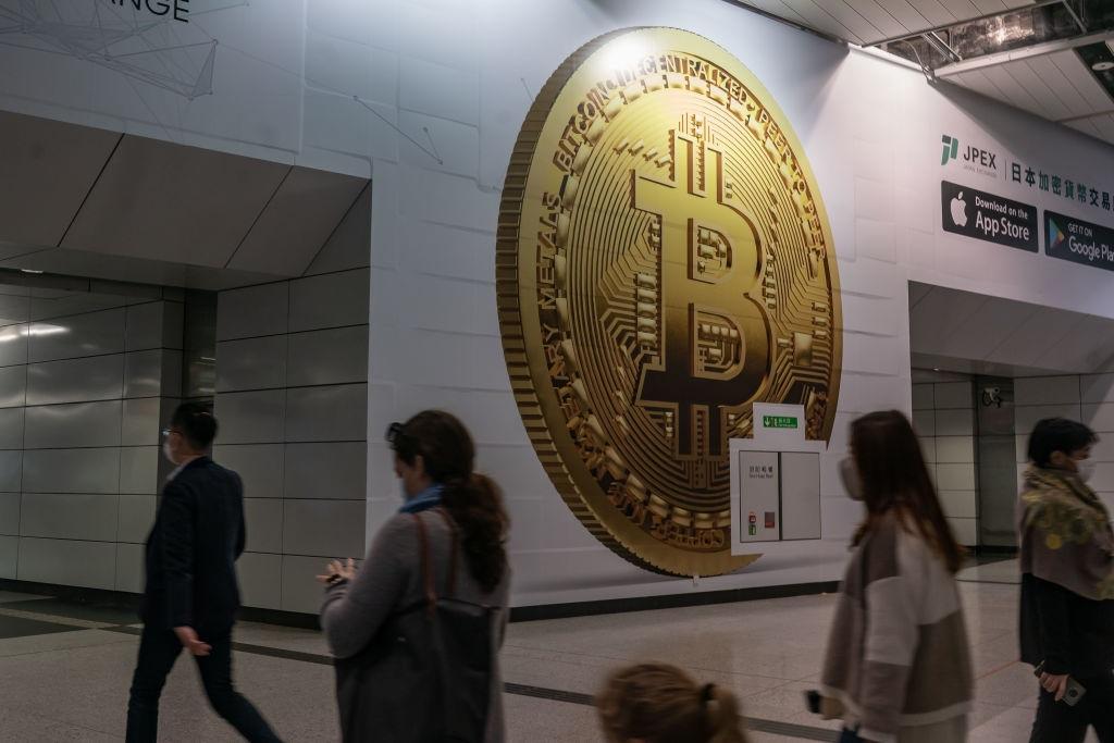 Pedestrians walk past an advertisement displaying a Bitcoin token