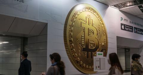 Pedestrians walk past an advertisement displaying a Bitcoin token