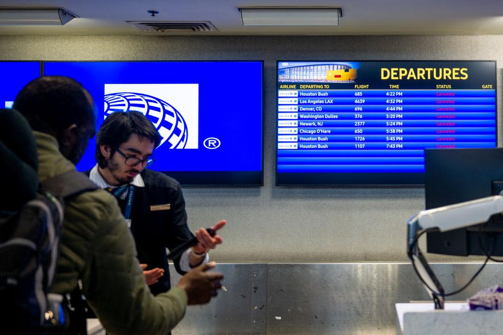 A United Airlines employee helping a passenger with a flight departures board behind them