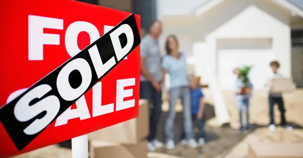 A house sits behind a for sale sign that is marked sold.