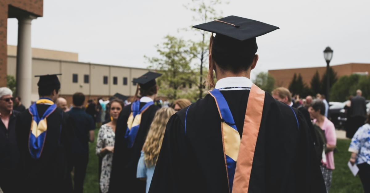 A student wears a graduation robe and hat as he stands looking away from the camera.