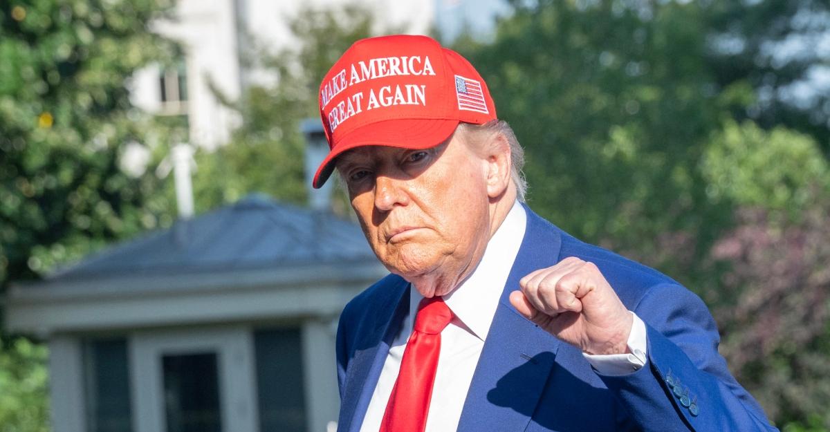 Trump wears a MAGA hat and holds up a fist