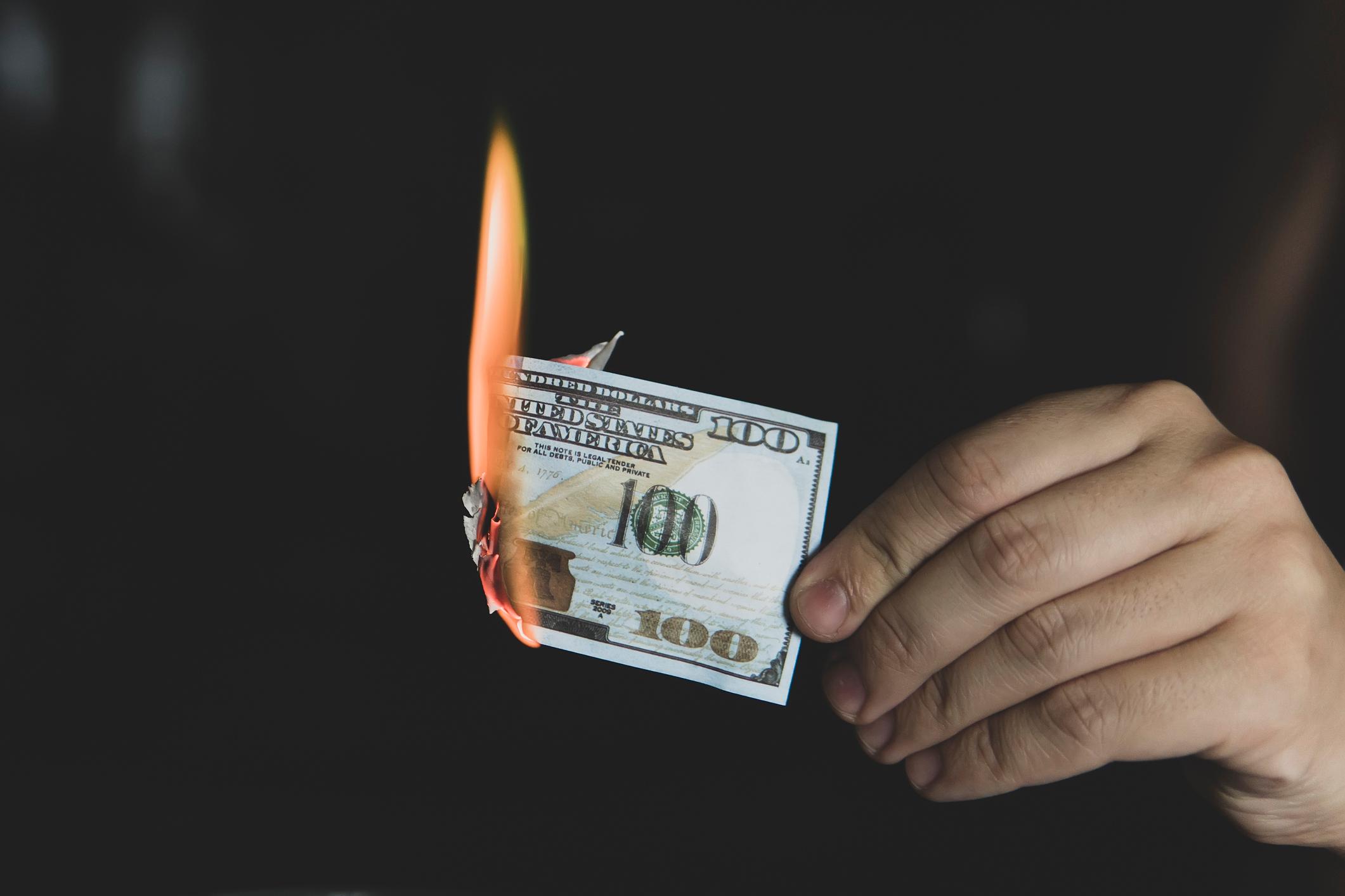 A $100 bill lit on fire being held against a black background