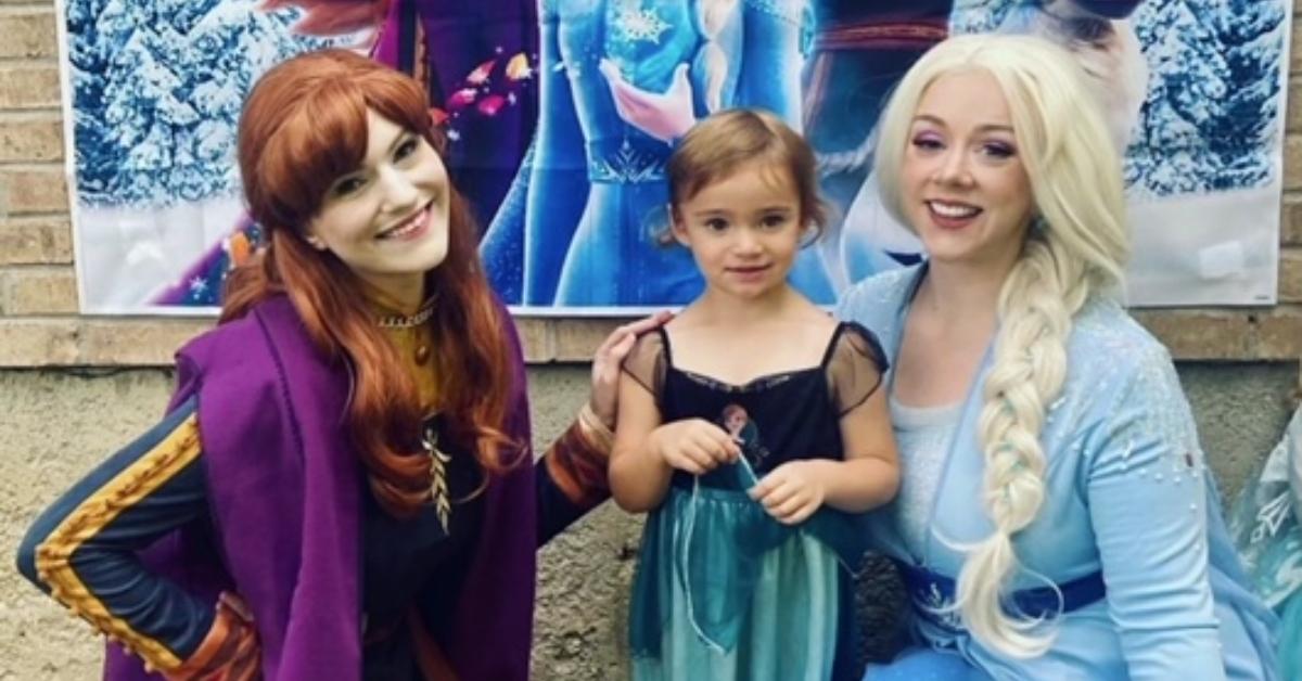 Two women dressed as 'Frozen' princesses Anna and Elsa with little girl.