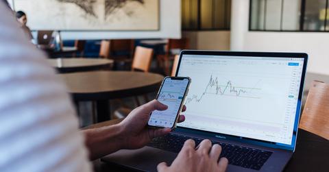 A person checking crypto prices on a phone and laptop