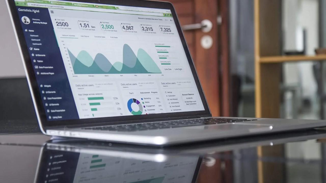 An open laptop sitting on a glass table with savings account stats on the screen.