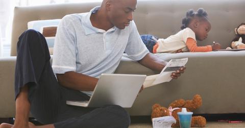 A father sitting on the floor looking at a document and a laptop