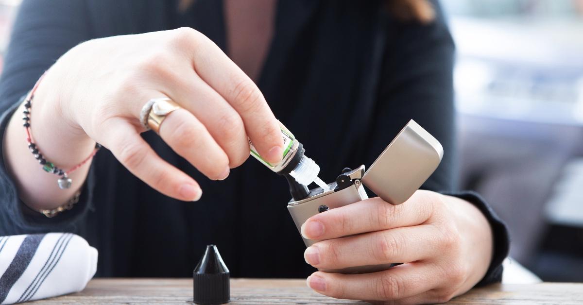 person pouring e-juice into vaping device