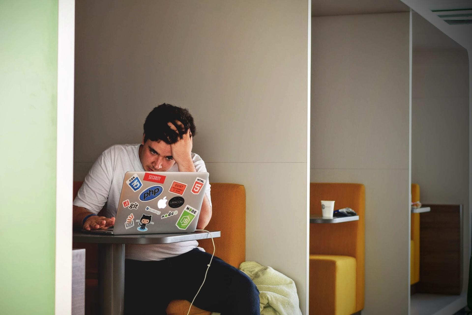 A man is seen looking at this laptop while sitting in a green-and-white booth on an orange couch