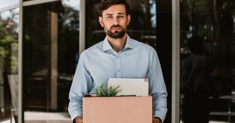 A man in a blue shirt leaves work with belongings after getting laid off.