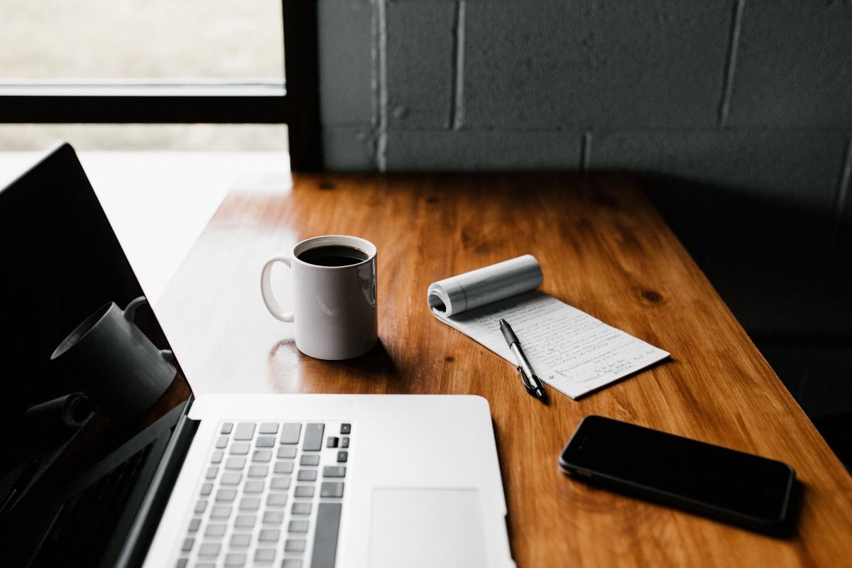 A laptop with notepad and coffee on a wooden desk