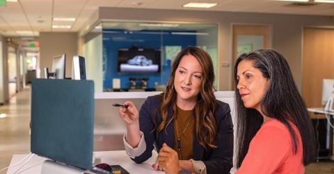 Two business women talking about sales in office at desk with laptop