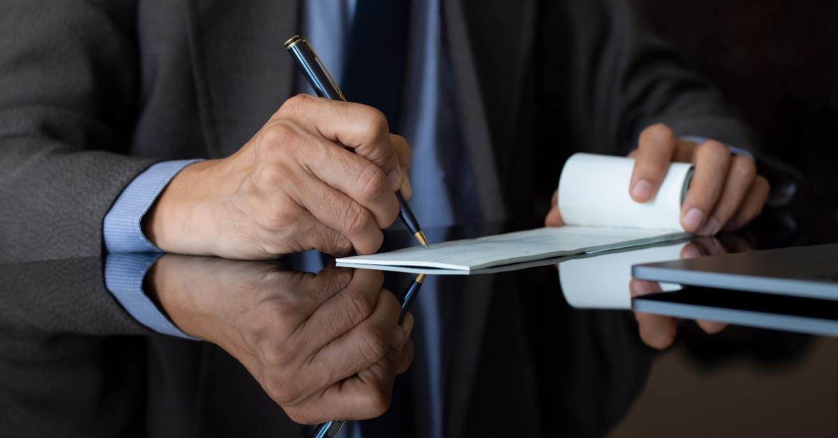 A close up of a businessman in a suit hand signing a check.