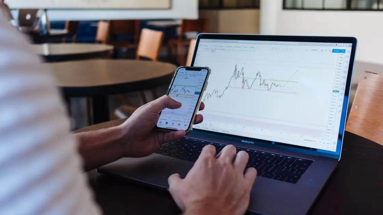 An man checking an investment app on his phone and using a laptop