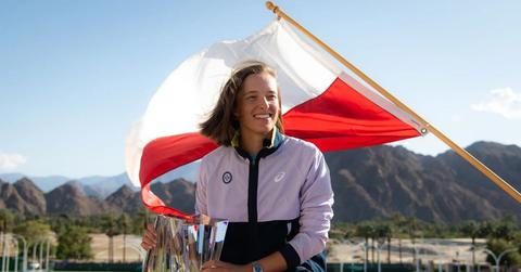 Polish tennis star Iga Swiatek poses in front of the Polish flag while holding the BNP Paribas Open trophy.
