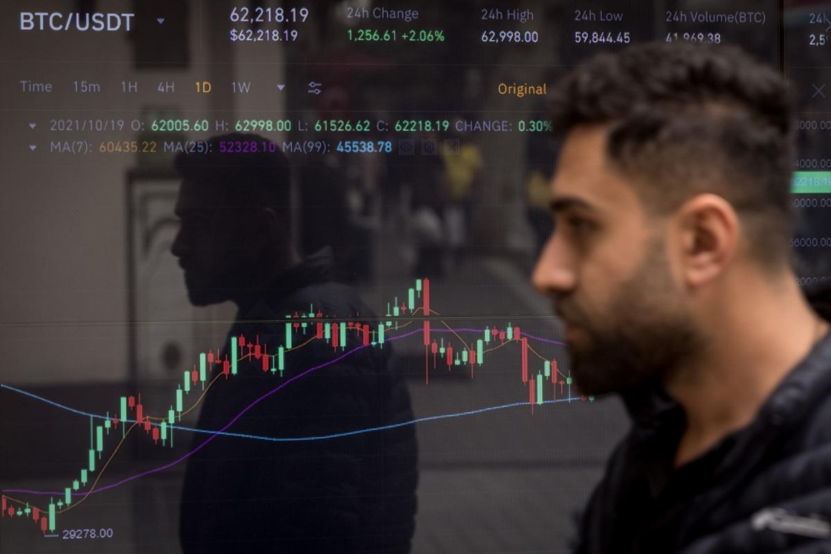 A person walks in front of a Bitcoin trading graph in a window of a cryptocurrency exchange office 