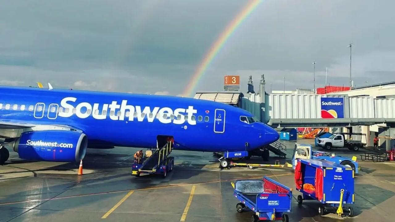 A Southwest plane parked at a gate with a rainbow behind it