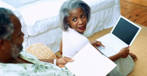 Older couple working on a laptop at home in their bedroom.