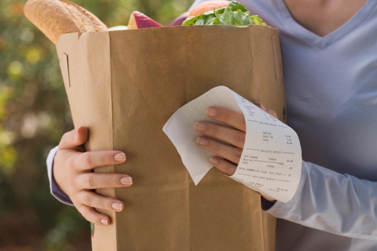 A woman carries a grocery bag and receipt.