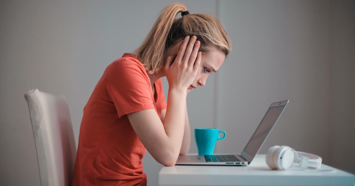 A concerned woman an in orange shirt looks at her computer. 