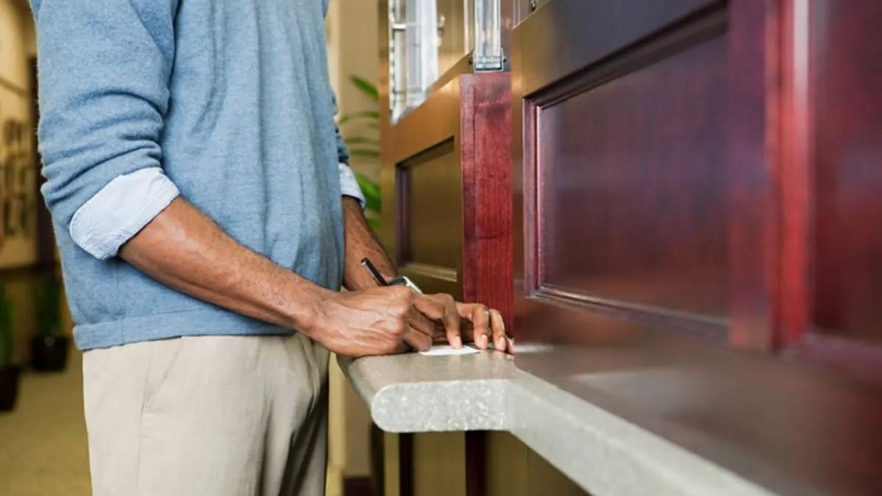 A man in a blue sweater filling out paperwork at a bank for certified funds