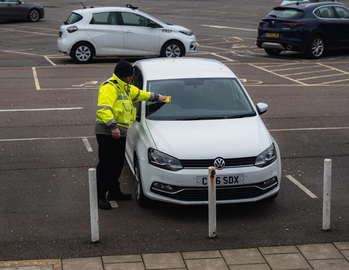 A parking officer places a parking ticket on a vehicle. 