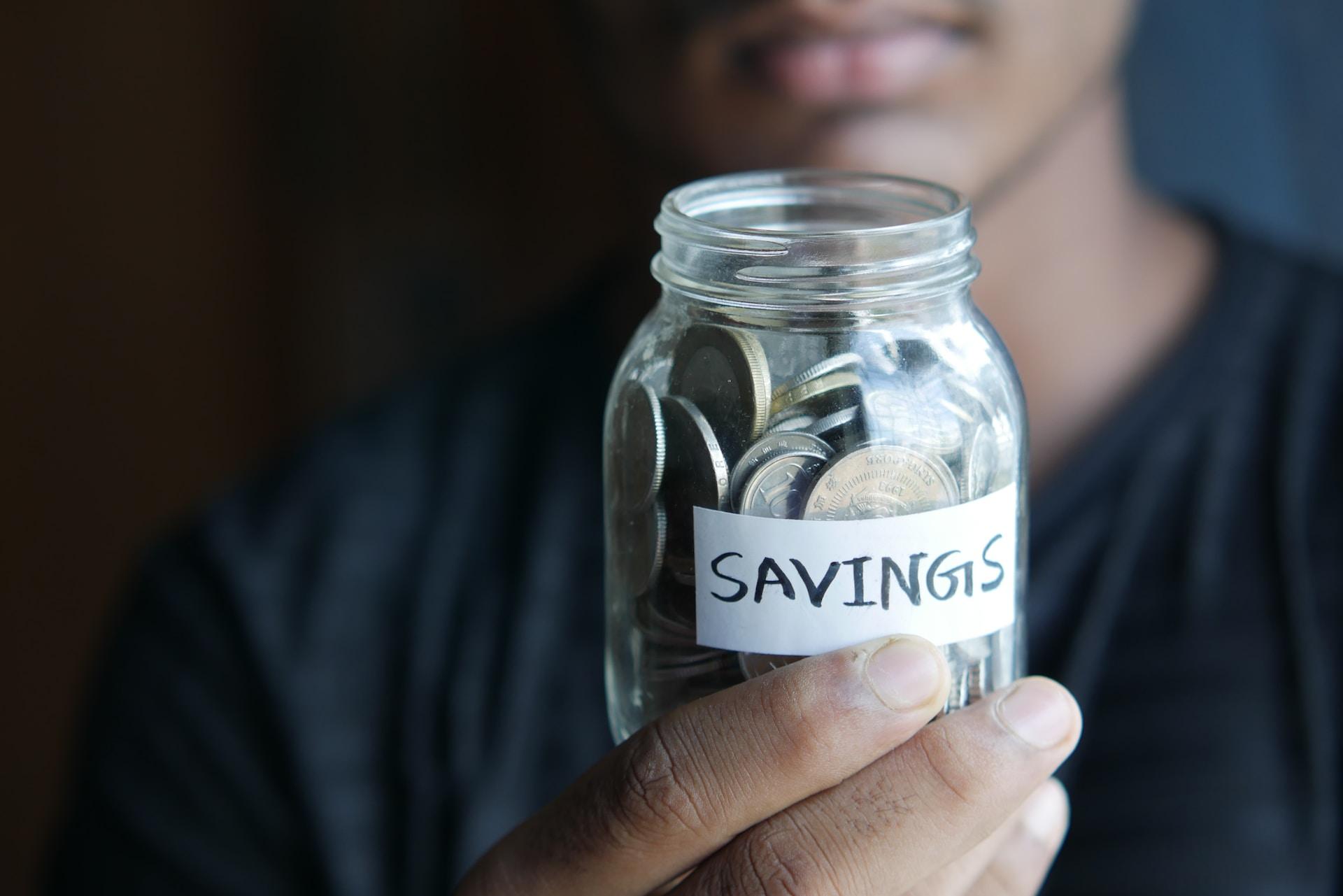 A man holding a mason jar with  savings label willed with loose coins