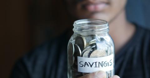 A man holding a mason jar with savings label willed with loose coins