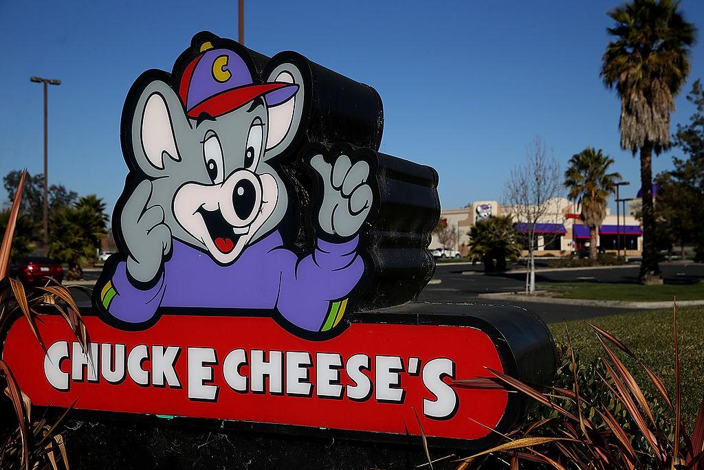 An Chuck E. Cheese's sign at the edge of a parking lot