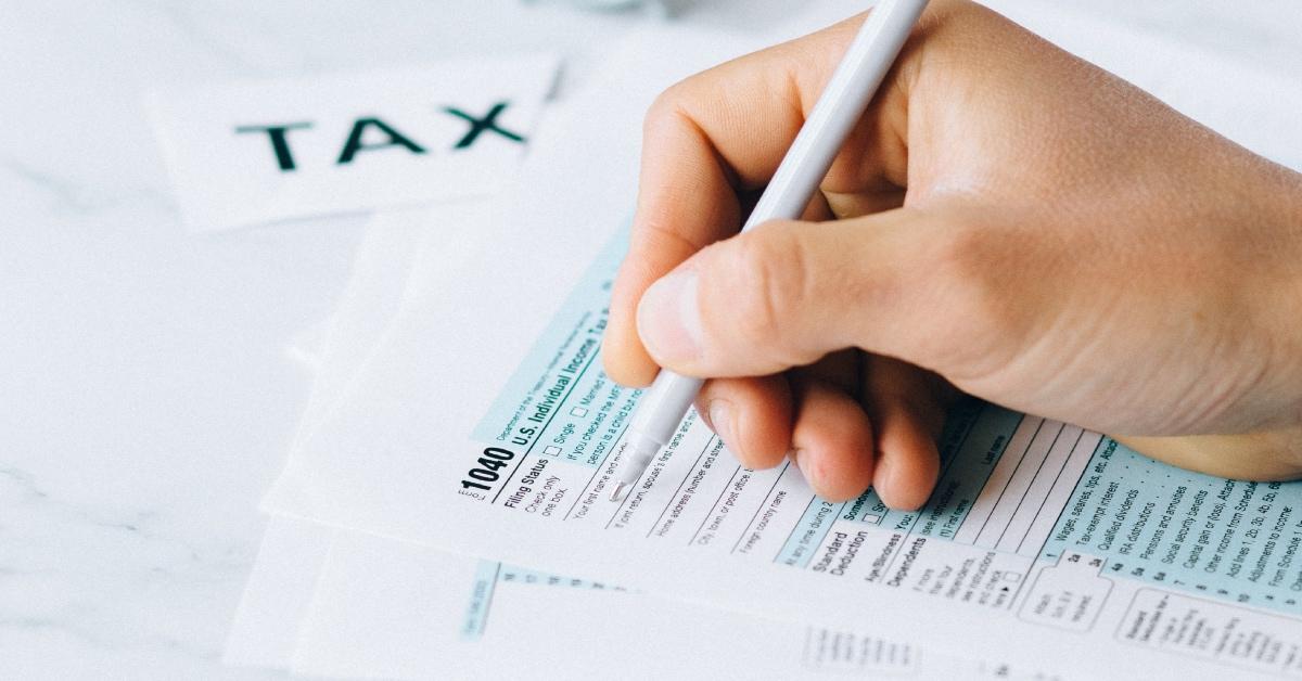 A person filling out a 1040 tax form sitting on a white table.