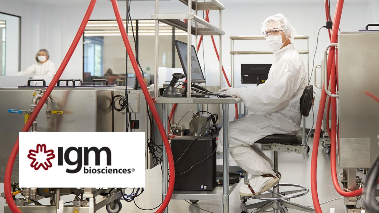 IGM Biosciences logo over scientist working in scrubs