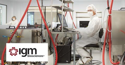 IGM Biosciences logo over scientist working in scrubs