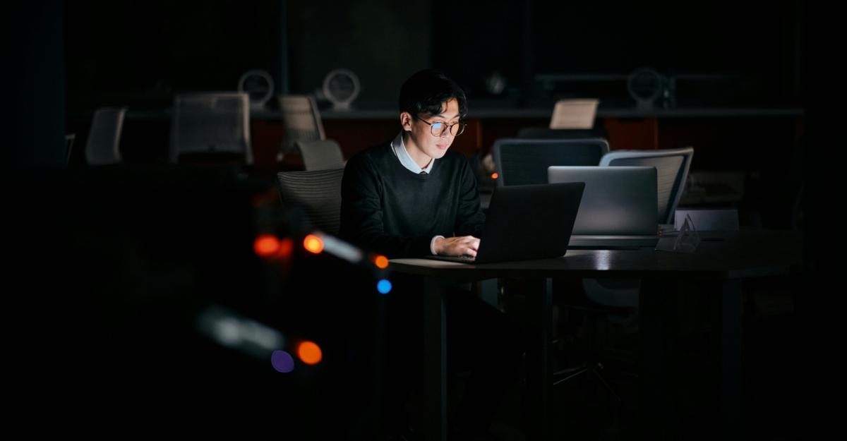 A man works on his laptop in a dark room.