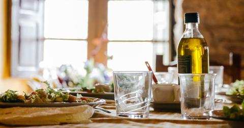 A bottle of olive oil on a table with a salad and glass of water