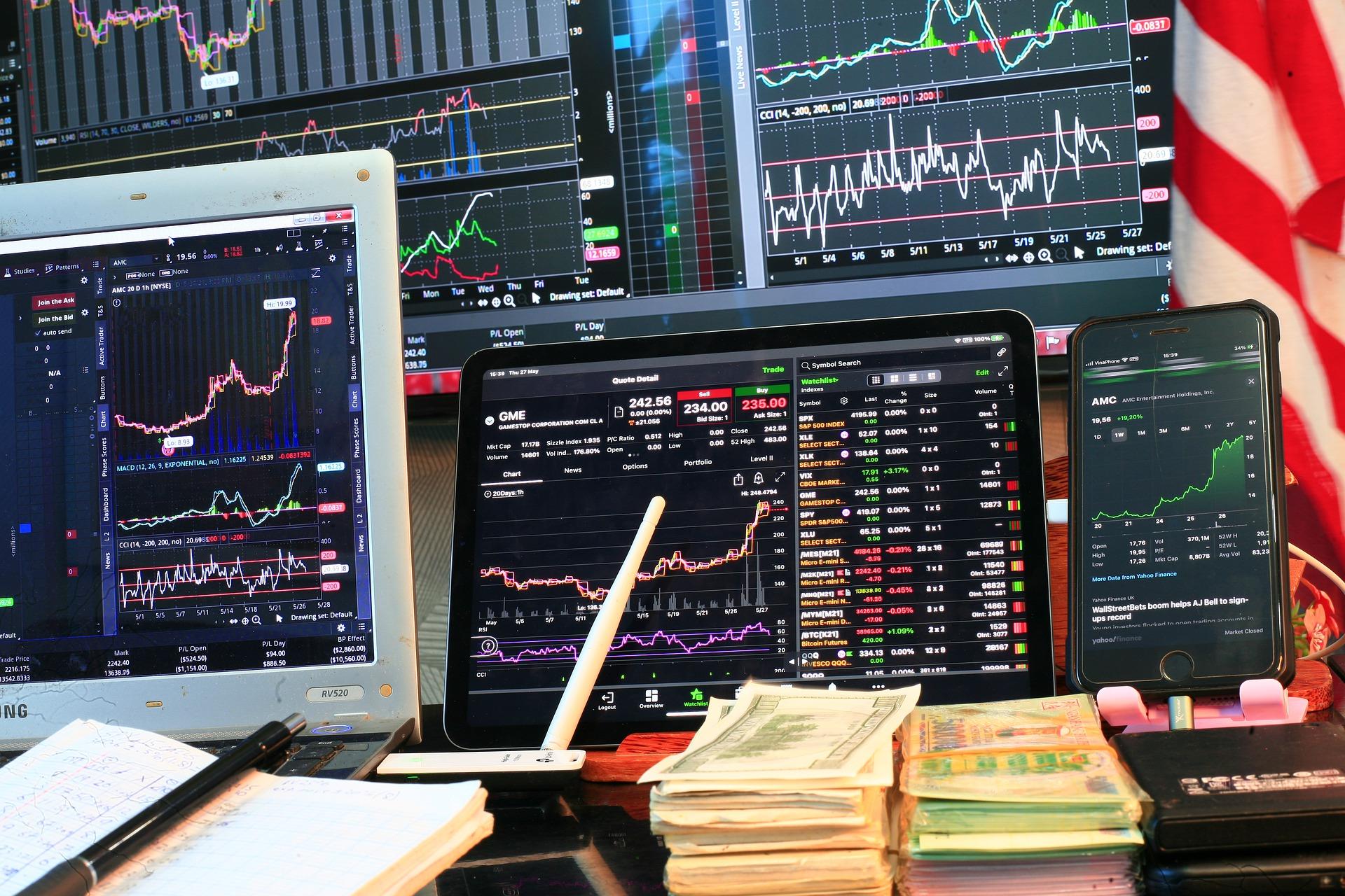 Stock prices displayed on screens along with a pile of cash