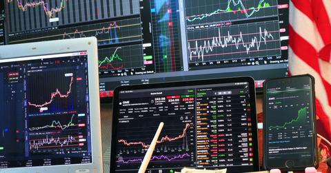 Stock prices displayed on screens along with a pile of cash