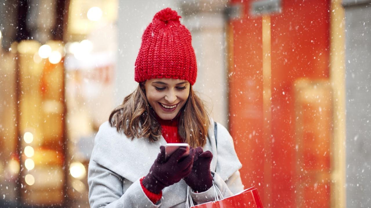 A young woman smiling while on her phone in the snow. 