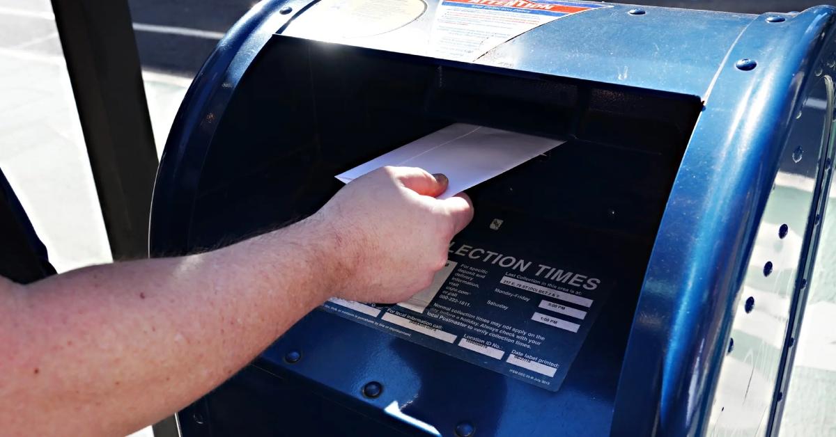 A person dropping an envelope into a blue USPS collection box.