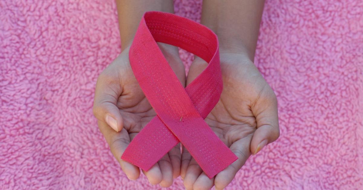 A person holding a pink breast cancer awareness ribbon