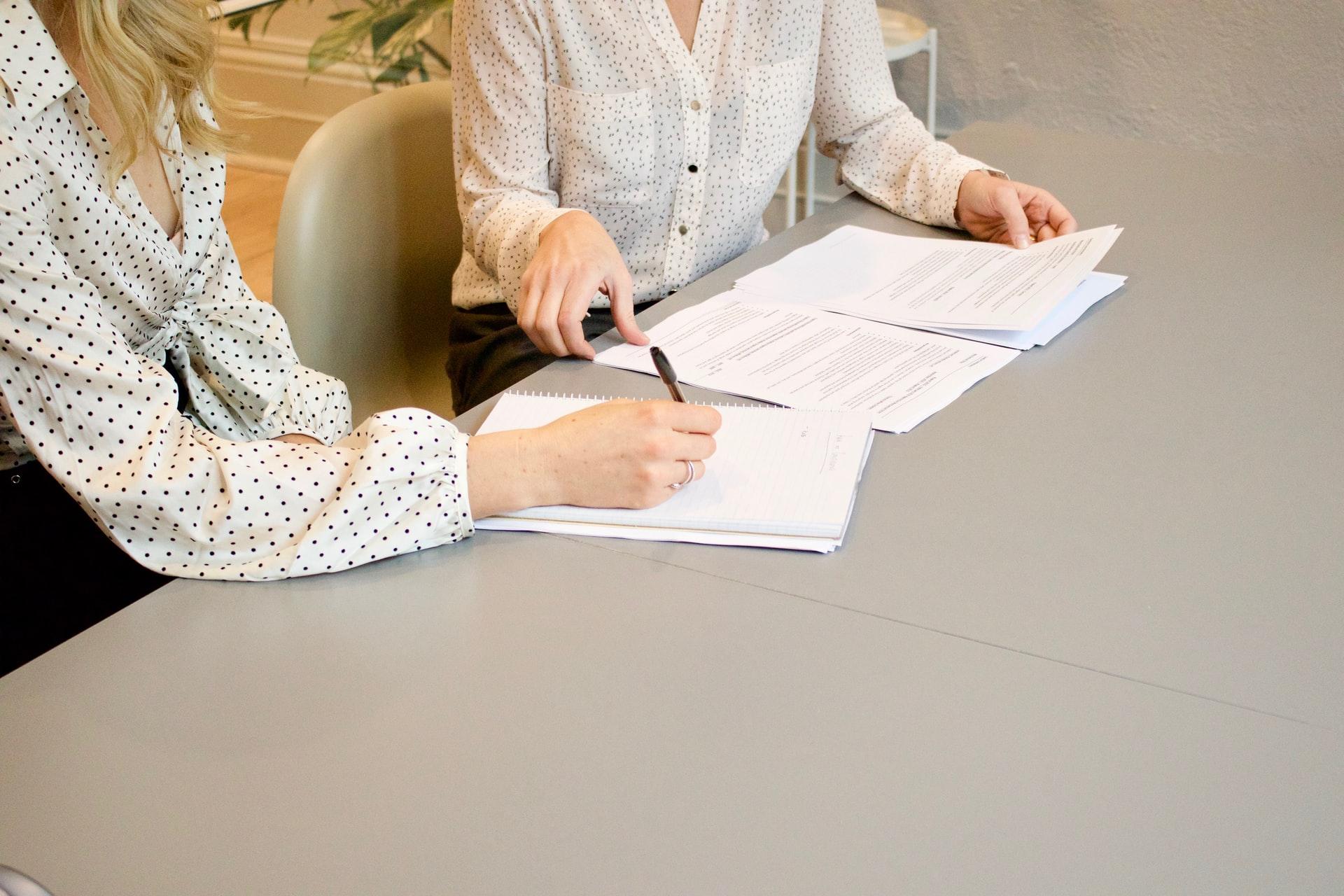 A woman signing papers while sitting beside another woman