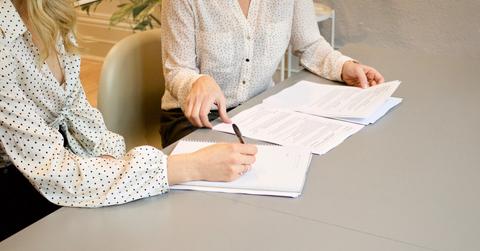 A woman signing papers while sitting beside another woman