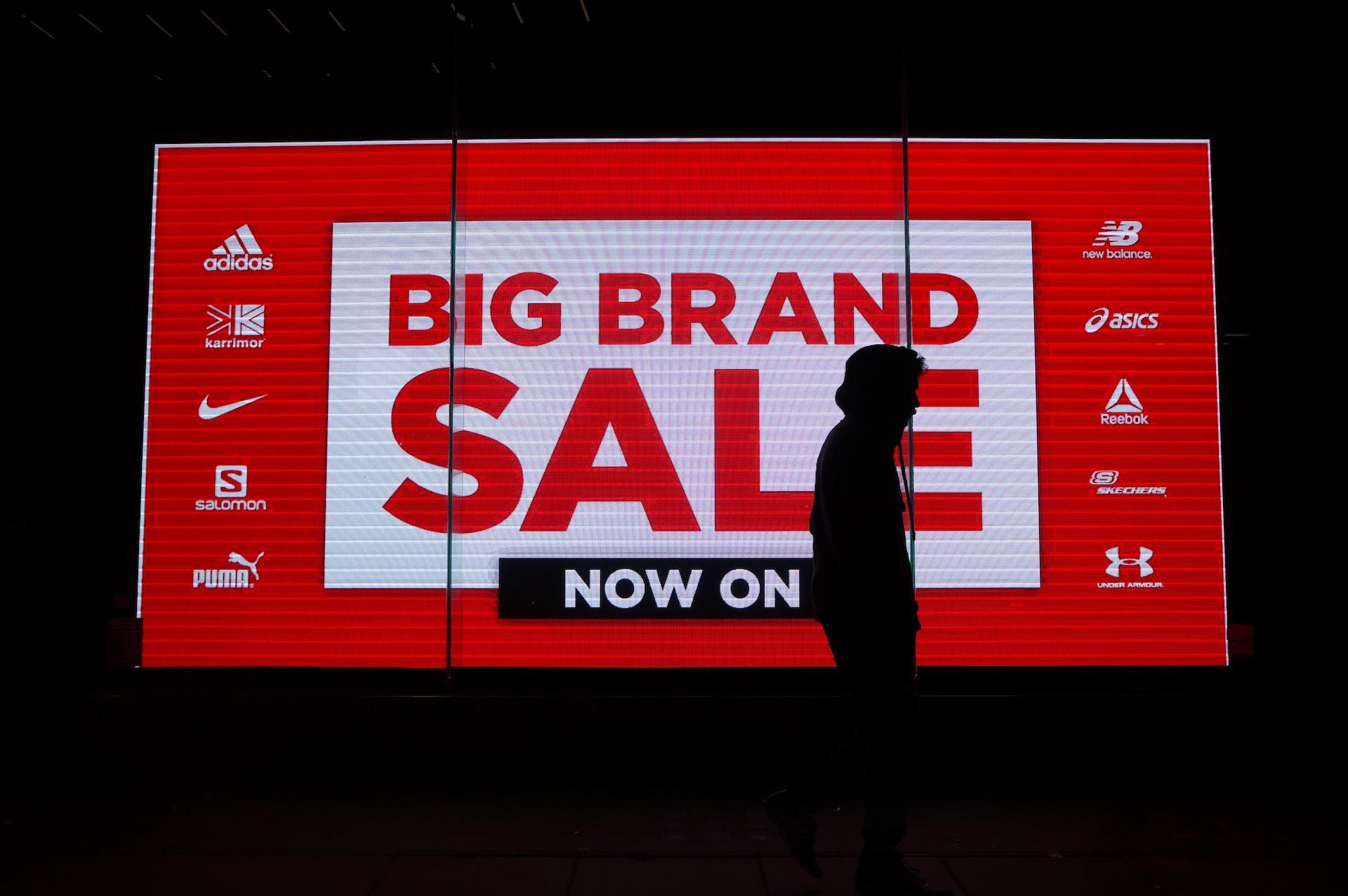 A person seen in front of a big brand sale sign advertising high-profile brand names 